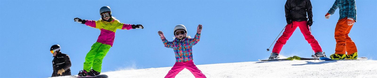 Children skiing and snowboarding on a sunny slope with adults behind them