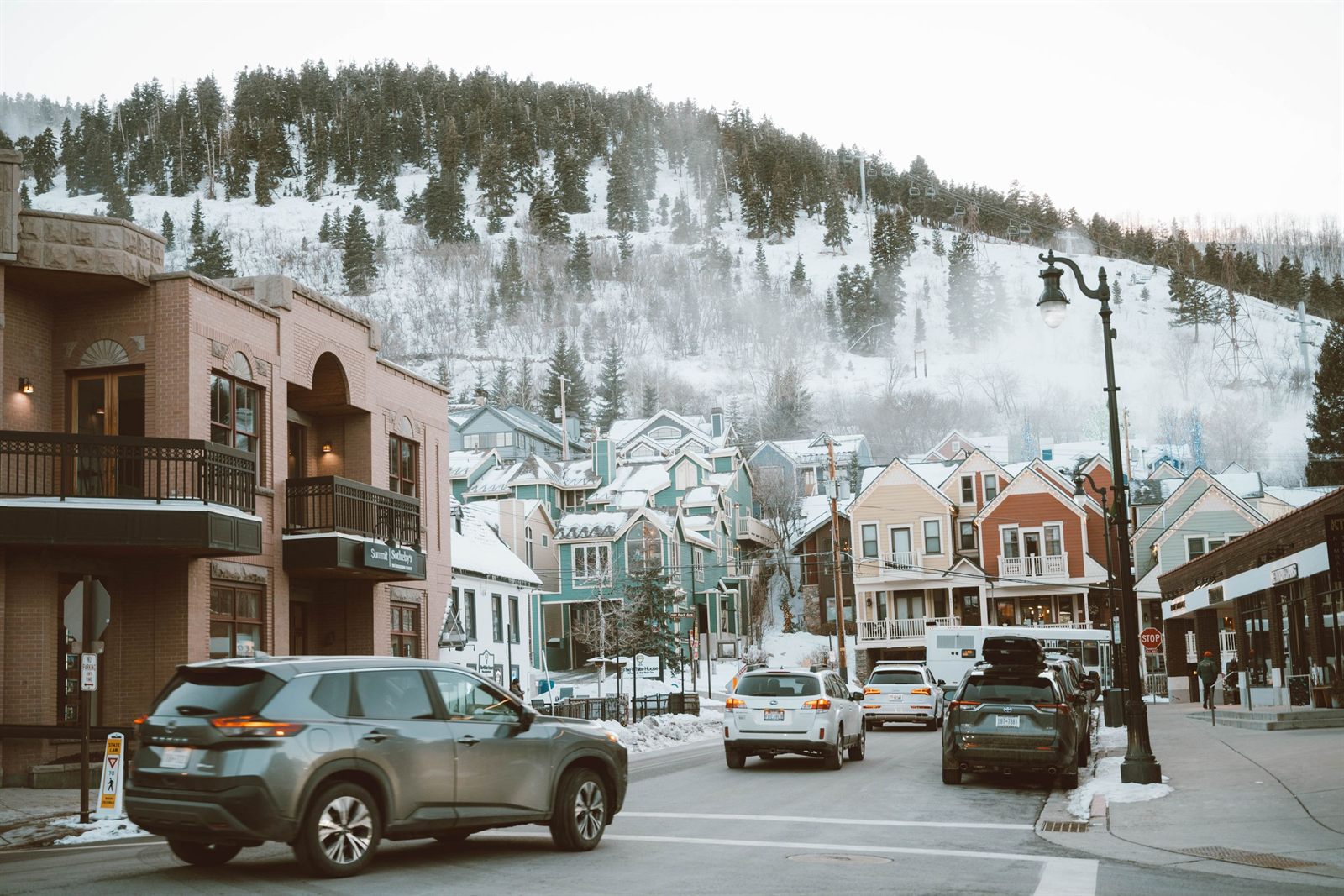 Snowy main street of a mountain town with colorful storefronts and a ski hill behind