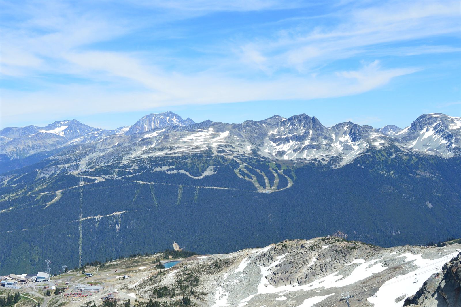 Ski runs cut through forested slopes below a long ridge of snowy peaks