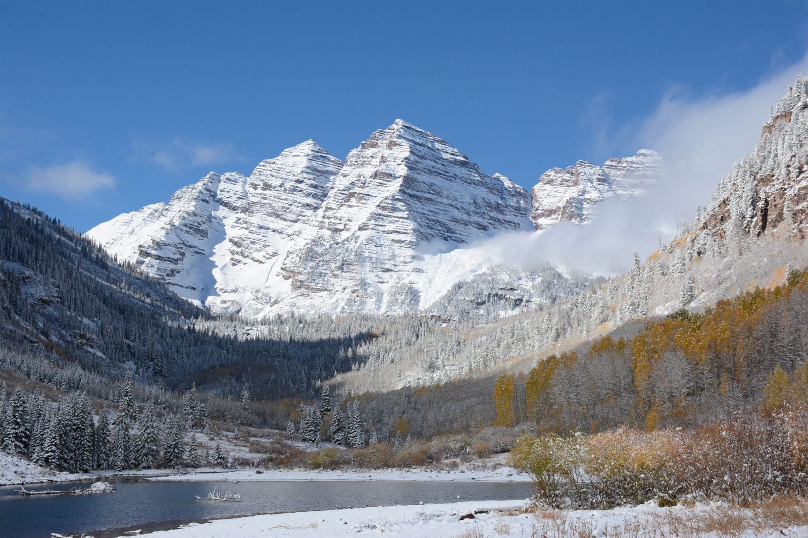 Snow-dusted twin peaks above a mountain lake and golden aspens in the Colorado Rockies